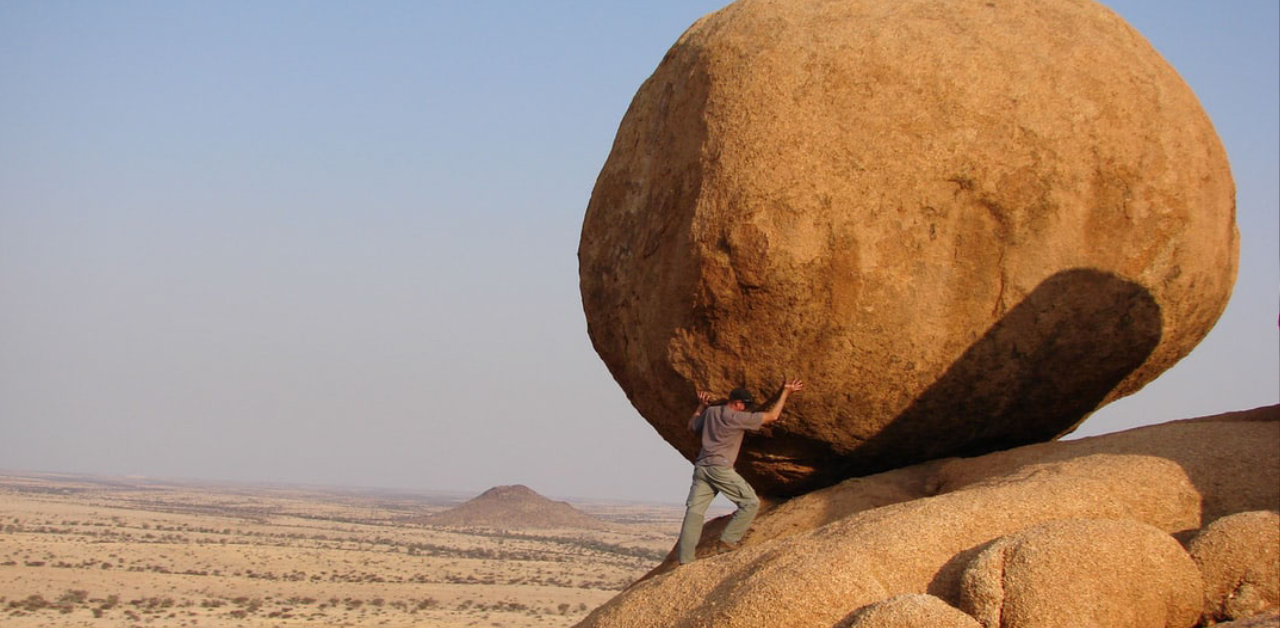 man pushing boulder in middle of desert